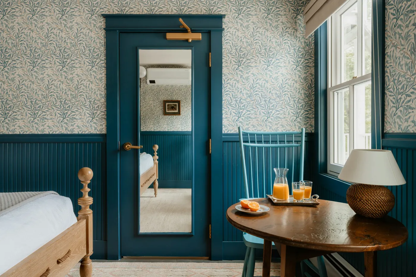 Kamer met wilgenbehang, een blauwe deur en een ronde houten tafel bij het raam