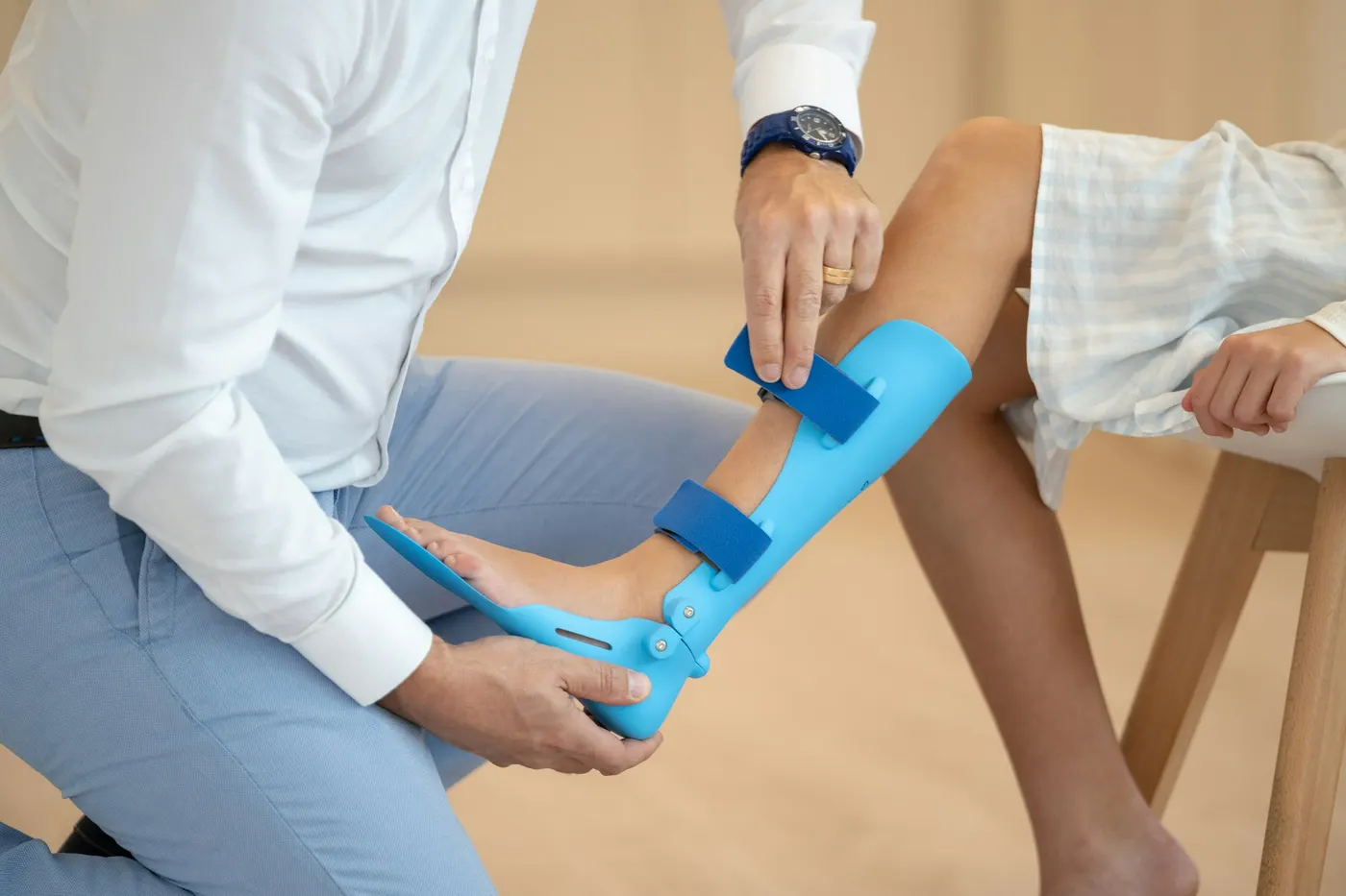 Een therapeut past een blauwe brace aan om het onderbeen en de voet van een cliënt