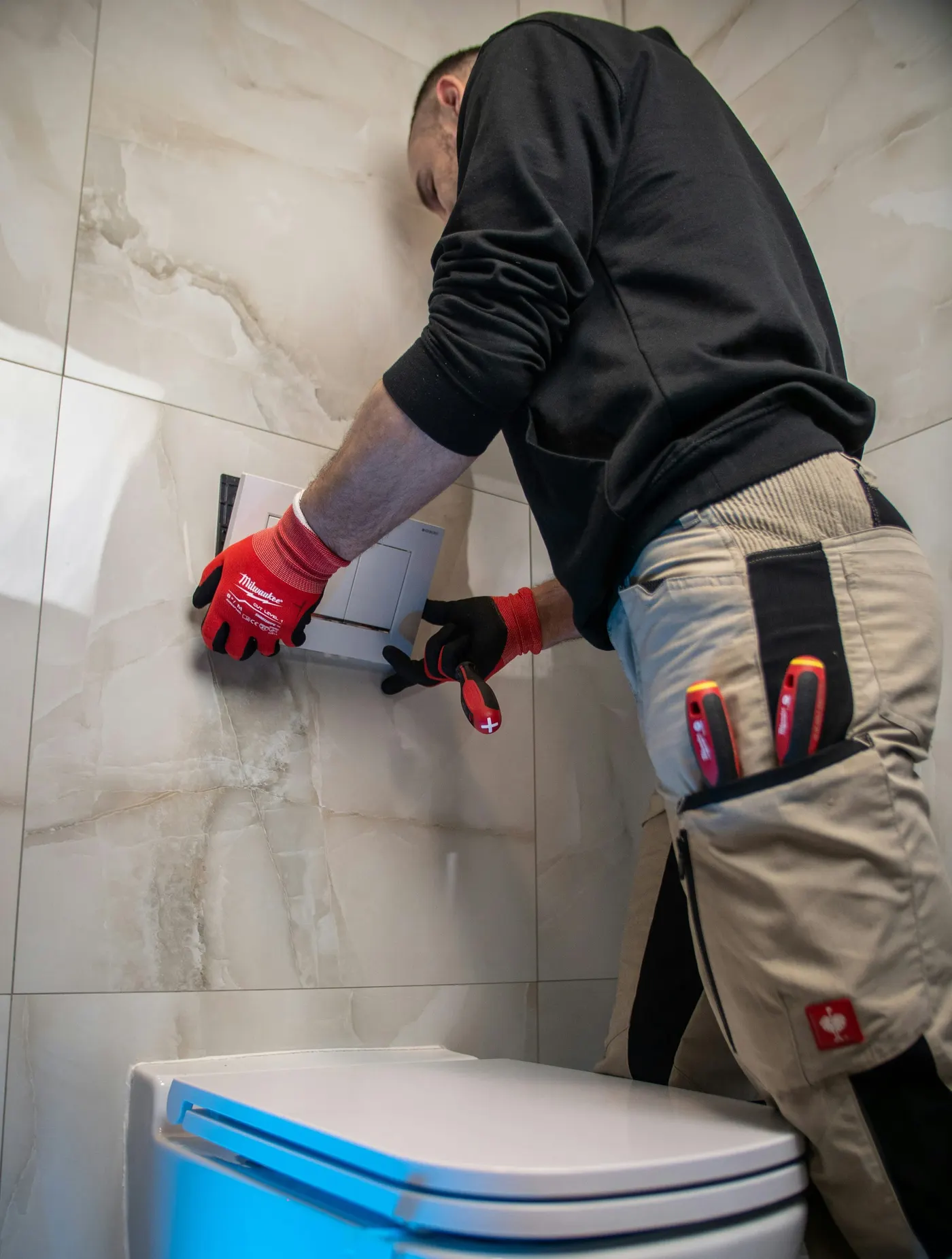 Een loodgieter monteert een inbouwreservoir en toiletknop tegen een betegelde wand